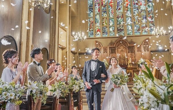 A newlywed couple in a church walk down the aisle as guests applaud and confetti falls from above.